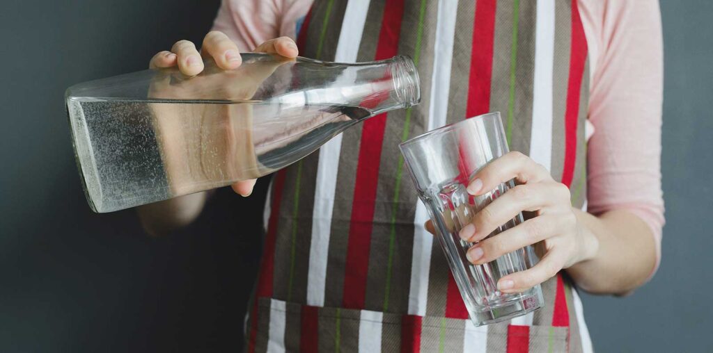 L'acqua potabile: i valori stabiliti dalla Legge Donna che versa acqua da bottiglia di vetro